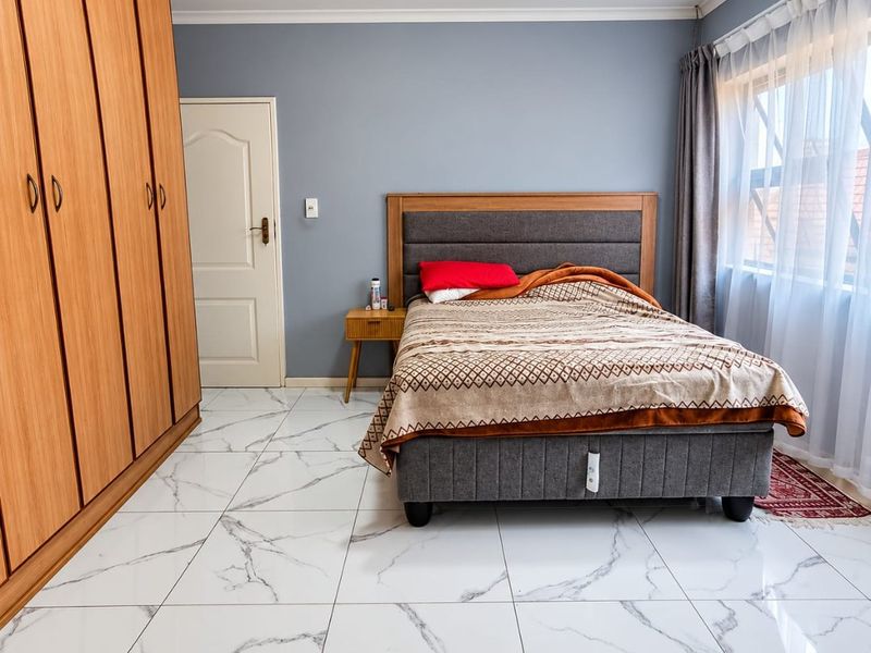 A well-maintained bedroom featuring modern marble-look floor tiles, a large built-in wooden wardrobe, and neutral grey wall finishes.