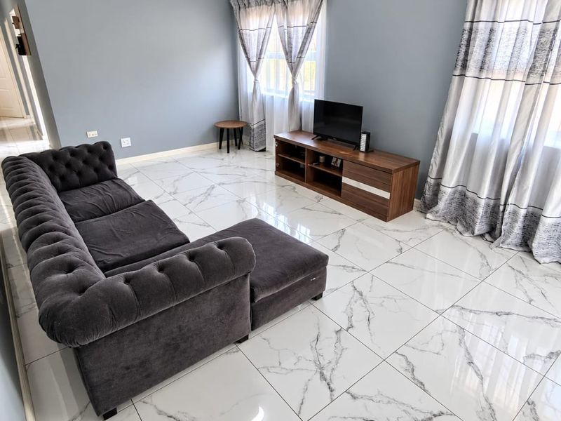 A bright living room featuring polished marble-look floor tiles, neutral grey walls, and large windows with natural light.
