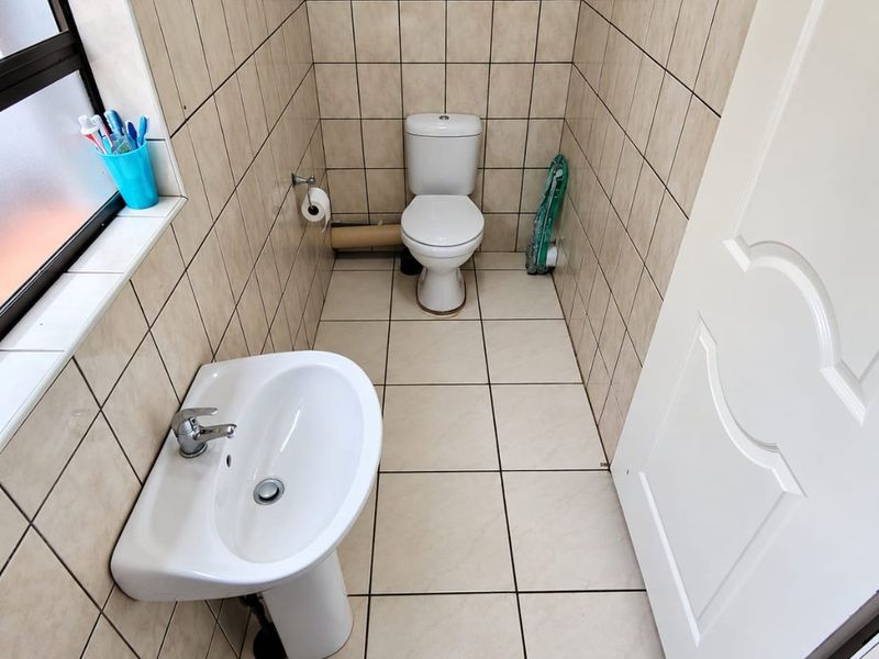 A compact bathroom featuring a pedestal washbasin, toilet, and neutral ceramic tiling throughout.