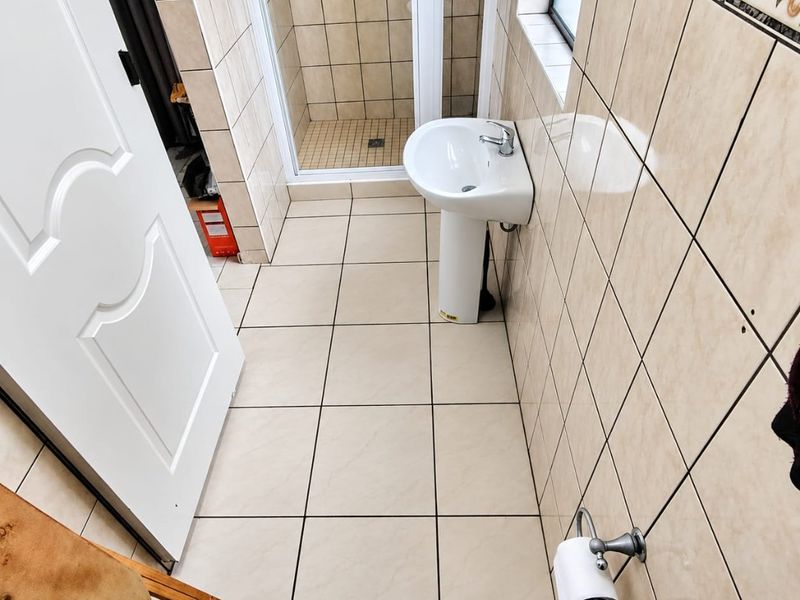 A functional bathroom featuring a pedestal basin, a tiled shower enclosure, and neutral wall and floor tiling throughout.