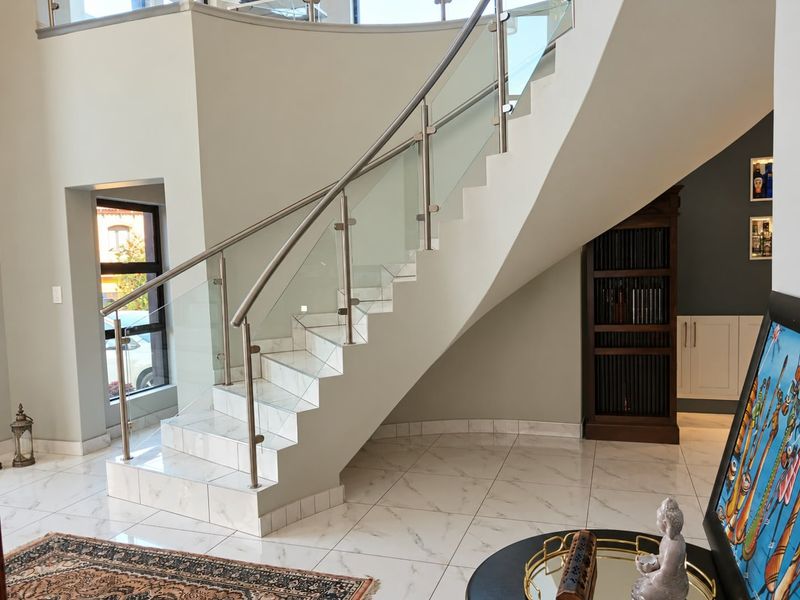 Elegant entrance hall featuring a striking curved staircase with a modern glass balustrade and polished marble-look floor tiles.
