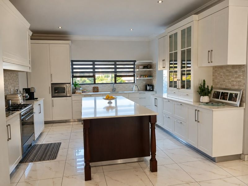 Modern, well-appointed kitchen featuring a central island, stone countertops, high-end built-in appliances, and elegant glass-fronted cabinetry with polished tiled flooring.
