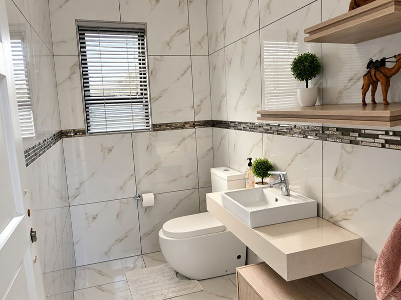 Modern bathroom featuring marble-look wall tiles, a sleek wall-mounted vanity with a vessel sink, and a back-to-wall toilet.