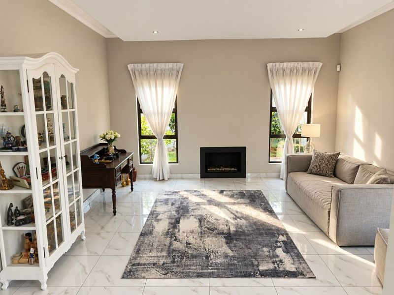 A bright and modern living room featuring polished marble-look floor tiles, a sleek built-in fireplace, and large windows with elegant curtains.
