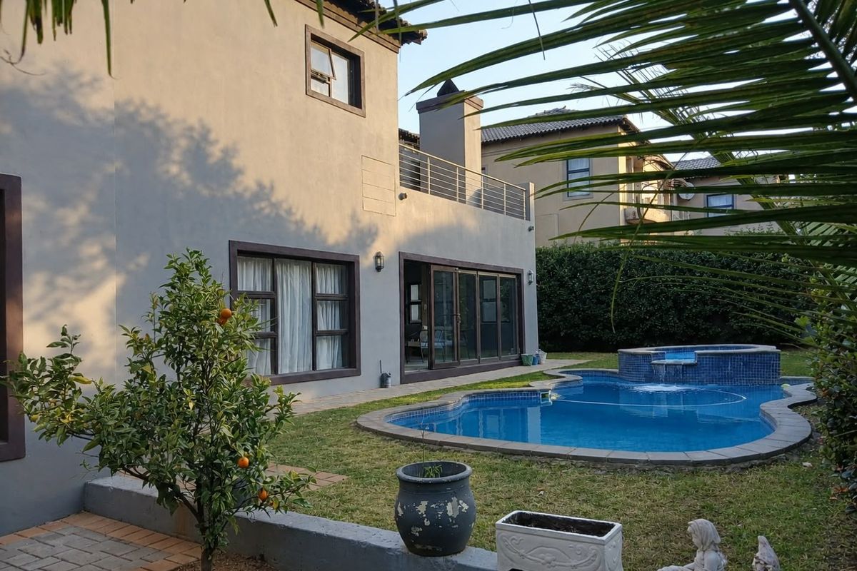 Rear view of the property featuring a swimming pool with a raised water feature, a paved patio, and an upper-level balcony with metal railings.