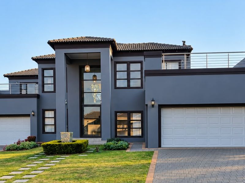 Modern double-story residence featuring a striking grey facade, double and single garages, expansive glass entrance, and upper-level balconies with metal railings.
