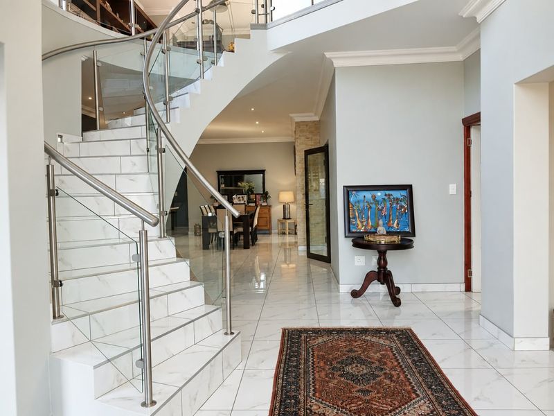 Elegant entrance hall featuring a striking curved staircase with glass balustrades and polished marble-look floor tiles, leading into an open-plan living area.