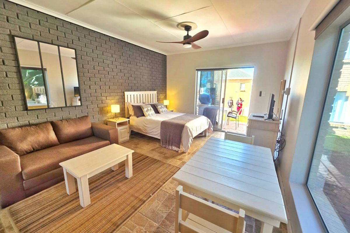 Spacious bedroom featuring an exposed brick accent wall, tiled flooring, and large sliding glass doors providing direct access to the outdoor area.