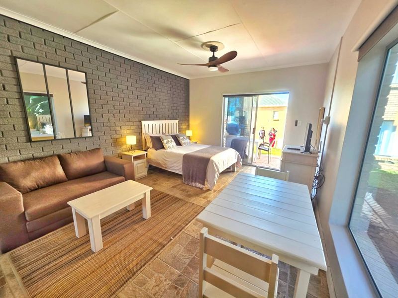 Spacious bedroom featuring an exposed brick accent wall, tiled flooring, and large sliding glass doors providing direct access to the outdoor area.