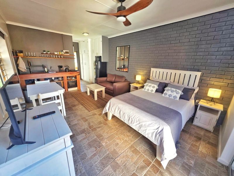 An open-plan studio apartment featuring a combined bedroom and kitchen area with tiled floors, an exposed brick feature wall, and a ceiling fan.