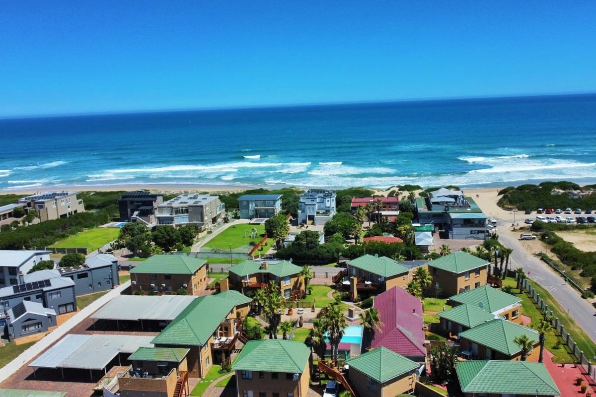 Aerial view of a coastal apartment complex featuring communal gardens, swimming pool, and parking facilities, situated in close proximity to the beach.