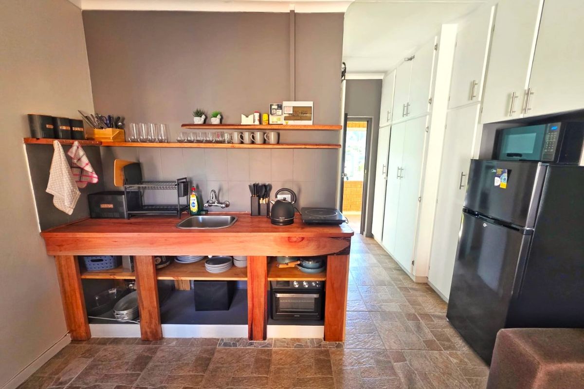 A compact kitchen featuring a rustic wooden countertop, open shelving, tiled flooring, and ample built-in storage cabinetry.