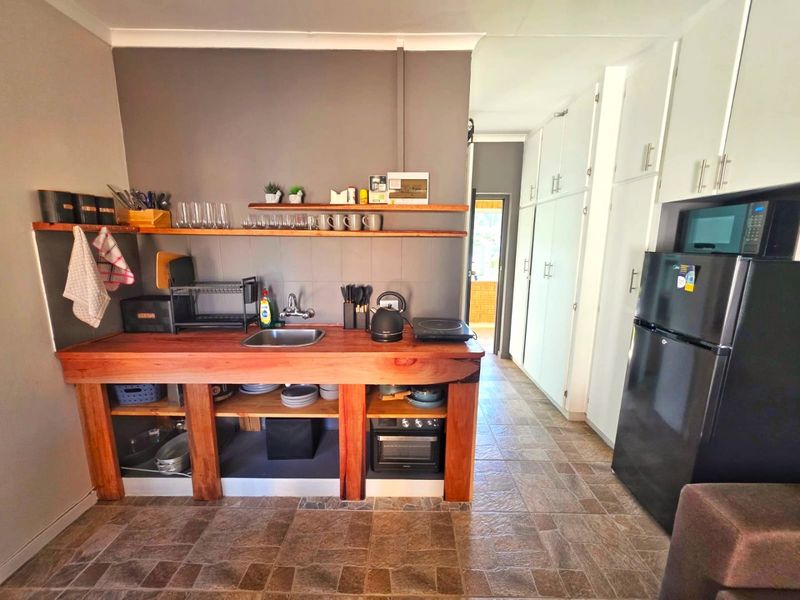 A compact kitchen featuring a rustic wooden countertop, open shelving, tiled flooring, and ample built-in storage cabinetry.