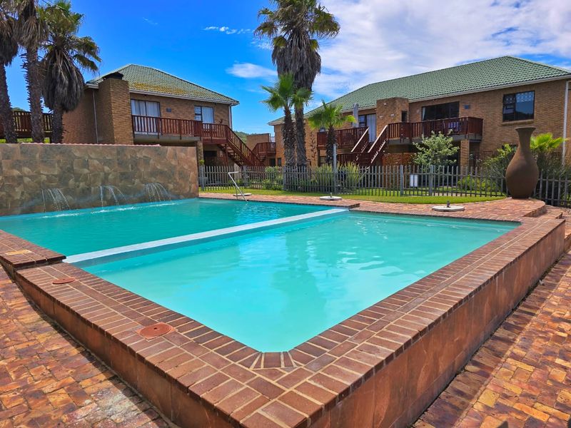 Communal swimming pool area featuring a water feature, brick paving, and views of the surrounding apartment complex buildings.