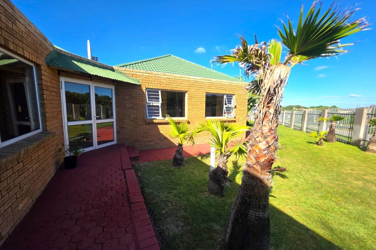 A view of the rear exterior of the apartment, featuring a brick facade, tiled roof, paved walkway, and a well-maintained garden area.