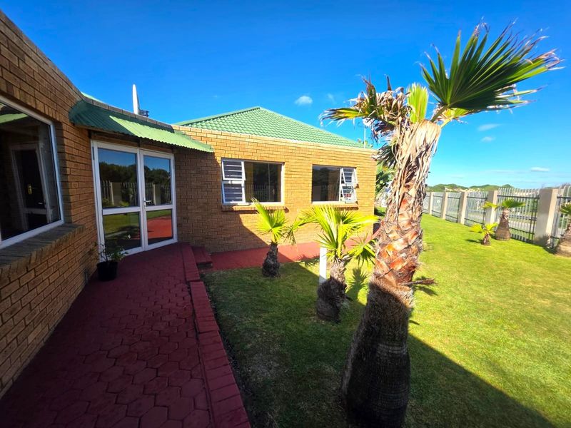 A view of the rear exterior of the apartment, featuring a brick facade, tiled roof, paved walkway, and a well-maintained garden area.