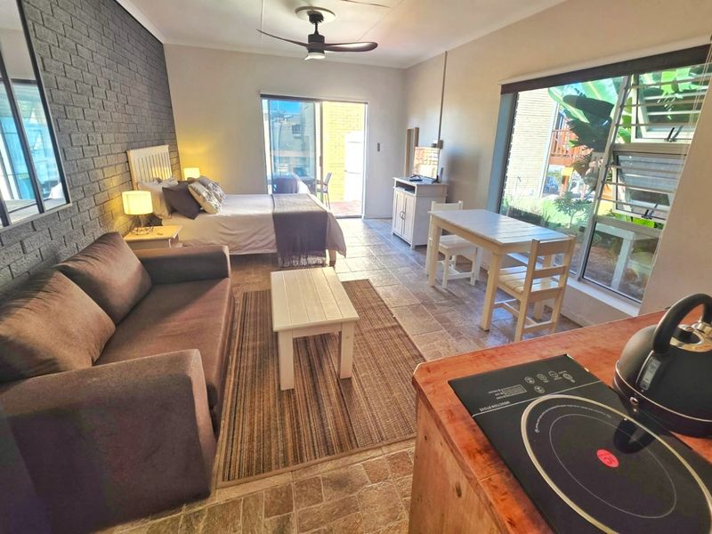 Open-plan studio apartment featuring a tiled living and sleeping area, exposed brick feature wall, ceiling fan, and direct access to an outdoor patio.
