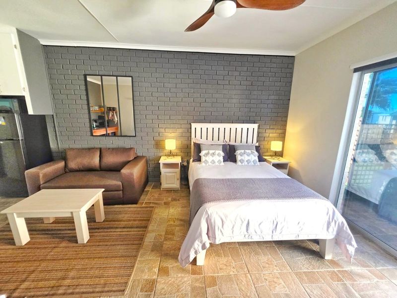 A well-lit bedroom featuring a distinctive grey exposed brick wall, tiled flooring, and a sliding glass door providing access to the exterior.
