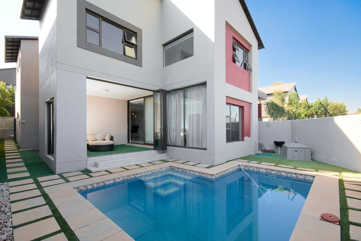 Rear view of the townhouse featuring a private swimming pool, paved surround, artificial lawn, and bi-fold doors leading into the living area.