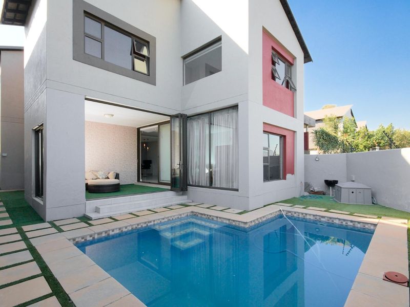 Rear view of the townhouse featuring a private swimming pool, paved surround, artificial lawn, and bi-fold doors leading into the living area.