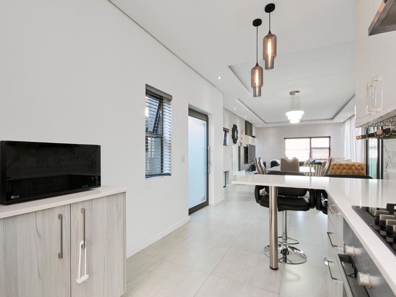 Modern open-plan kitchen and living area featuring sleek cabinetry, stone countertops, integrated appliances, and contemporary pendant lighting, creating a bright and cohesive living space.