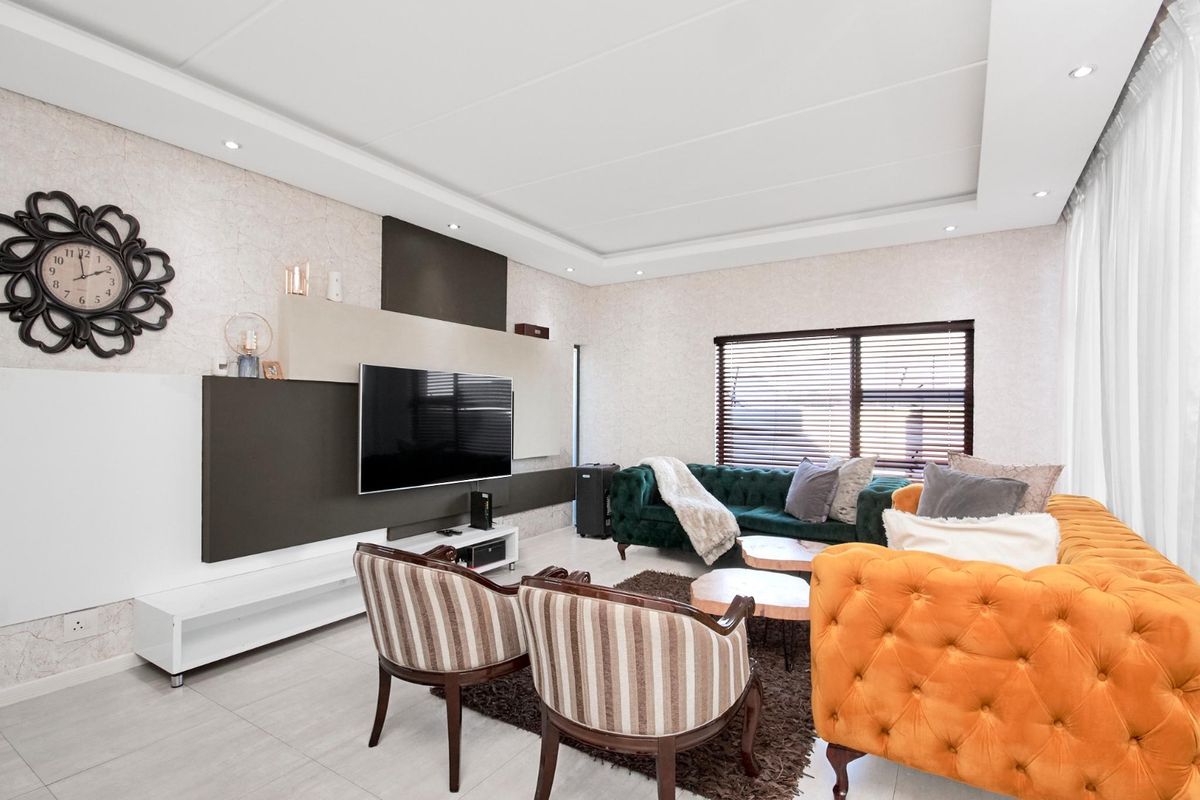 A modern living room featuring a custom built-in media wall, recessed ceiling with downlights, tiled flooring, and large windows with venetian blinds.