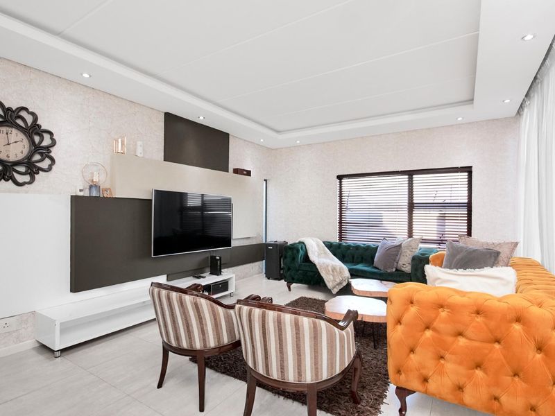 A modern living room featuring a custom built-in media wall, recessed ceiling with downlights, tiled flooring, and large windows with venetian blinds.