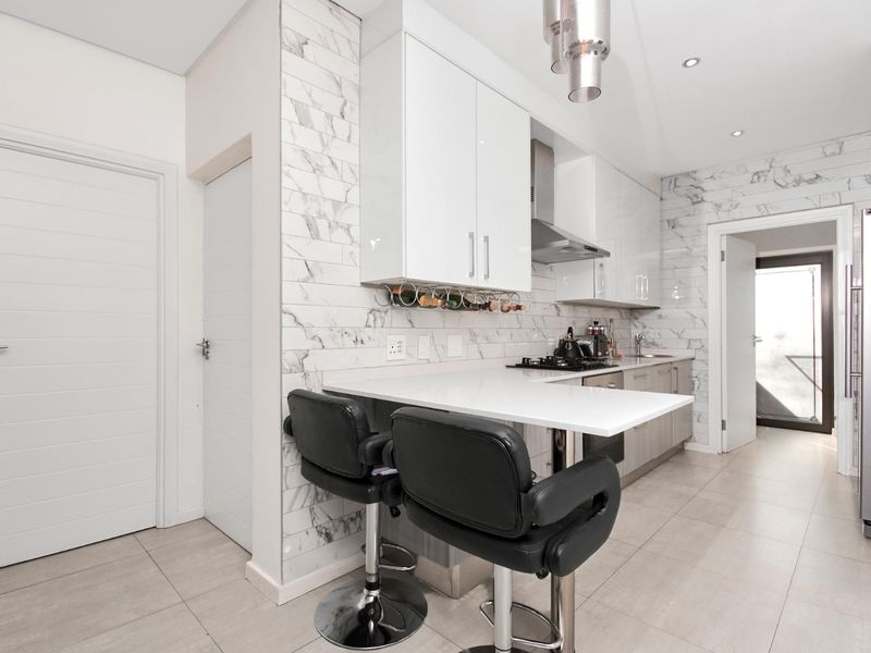 Modern kitchen featuring high-gloss white cabinetry, marble-look wall tiling, quartz countertops, and integrated gas hob with stainless steel extractor.
