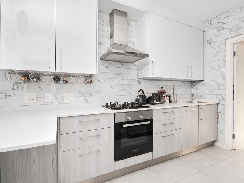 Modern kitchen featuring white gloss cabinetry, marble-look subway tile backsplash, stone countertops, and integrated stainless steel appliances including a gas hob and oven.