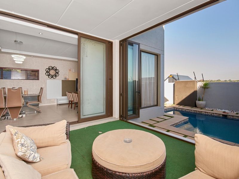 Covered patio area featuring seamless indoor-outdoor flow through large sliding and folding glass doors, overlooking a private swimming pool and landscaped garden.