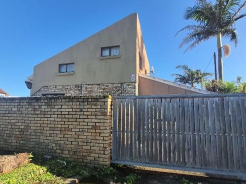 Front exterior view of a house featuring a brick boundary wall, timber sliding gate, and stone cladding facade under a clear blue sky.
