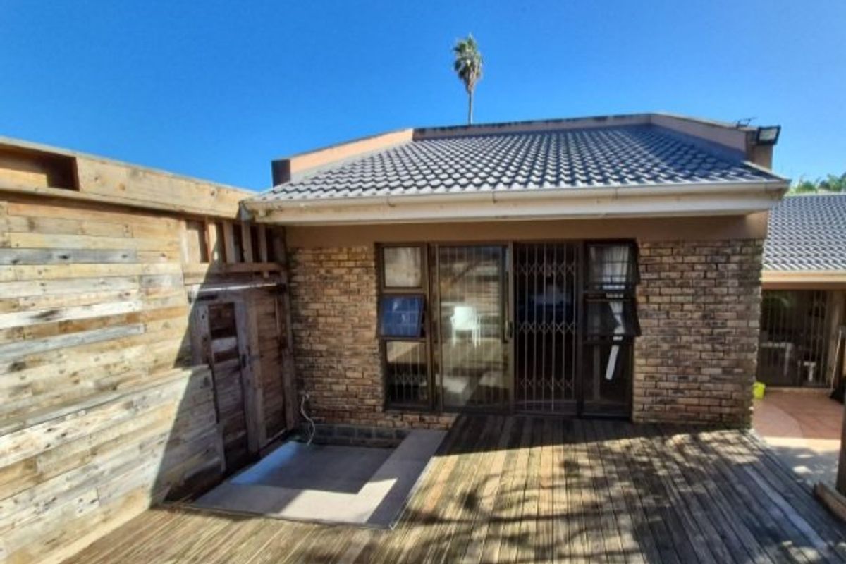 Rear exterior view featuring a timber deck, brick facade, and sliding glass doors with security gates.