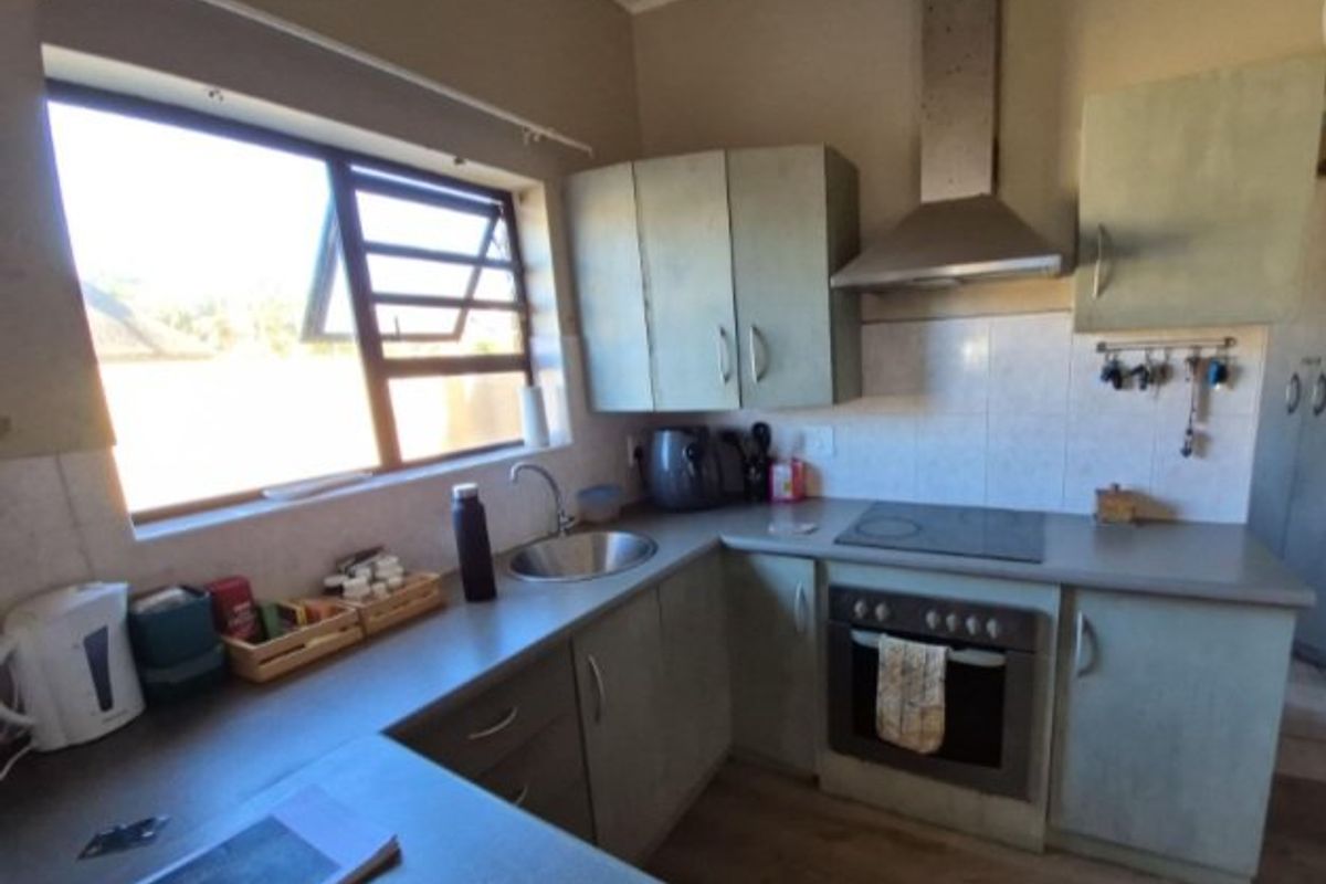 Functional kitchen featuring built-in cabinetry, laminate countertops, integrated electric hob and oven, stainless steel extractor fan, and tiled backsplash.