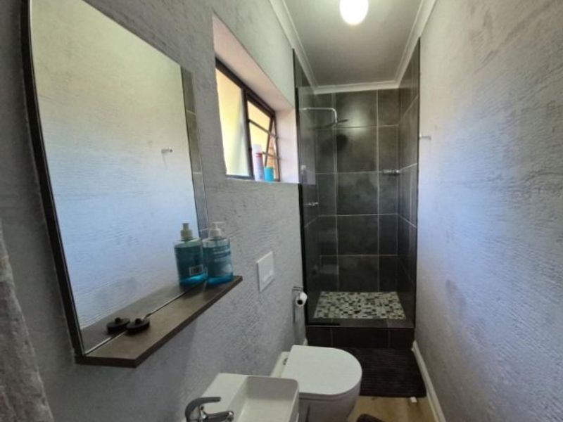 A modern bathroom featuring a walk-in shower with pebble tile flooring, a wall-mounted toilet, and a sleek vessel sink with a floating mirror.
