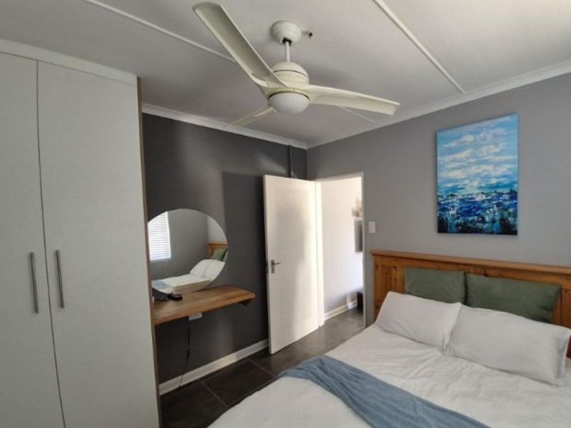A well-maintained bedroom featuring built-in cupboards, a ceiling fan, and a floating vanity shelf with tiled flooring.