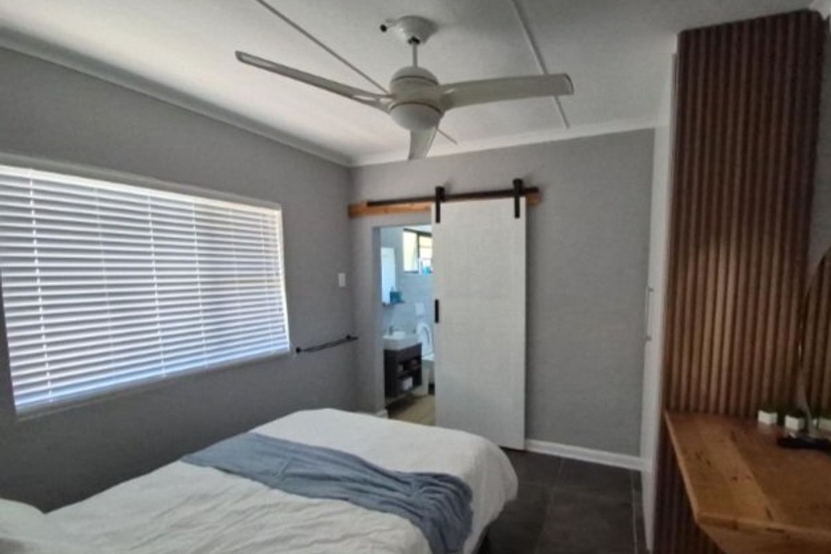 Modern bedroom featuring a ceiling fan, sliding barn door, venetian blinds, and a custom timber slat wall with an integrated built-in desk.