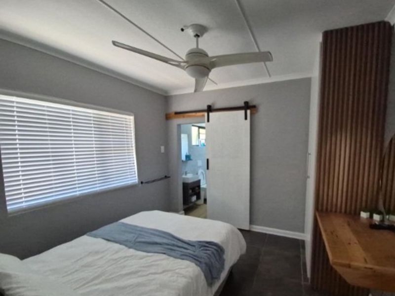 Modern bedroom featuring a ceiling fan, sliding barn door, venetian blinds, and a custom timber slat wall with an integrated built-in desk.