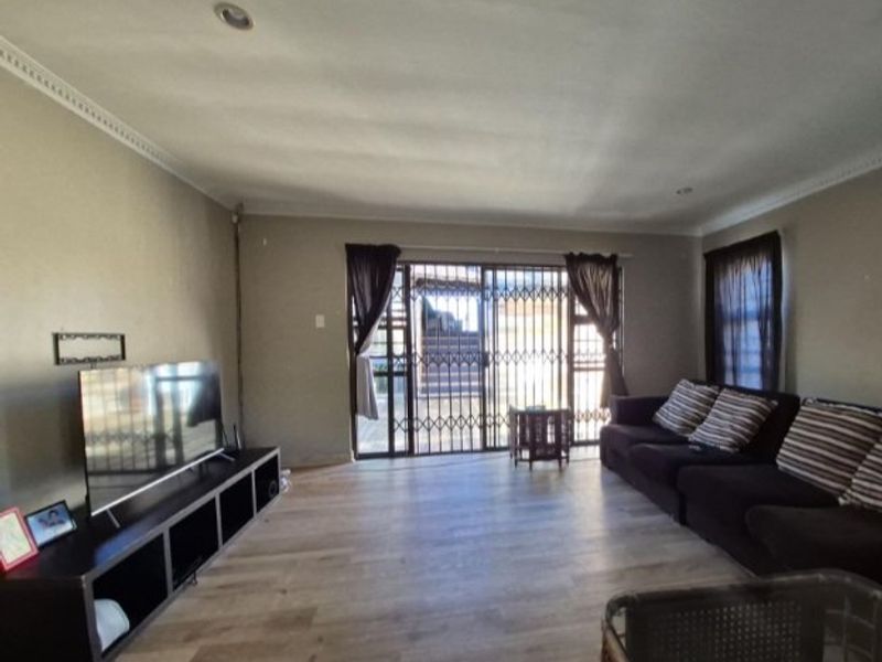A living room featuring laminate flooring, recessed lighting, and a sliding glass door with an integrated security gate leading to the exterior.