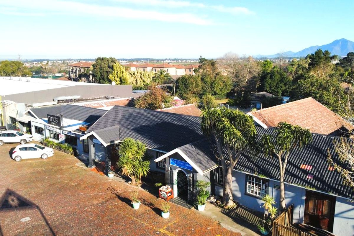Aerial view of a commercial property complex featuring multiple storefronts, tiled roofing, and an expansive paved parking area.