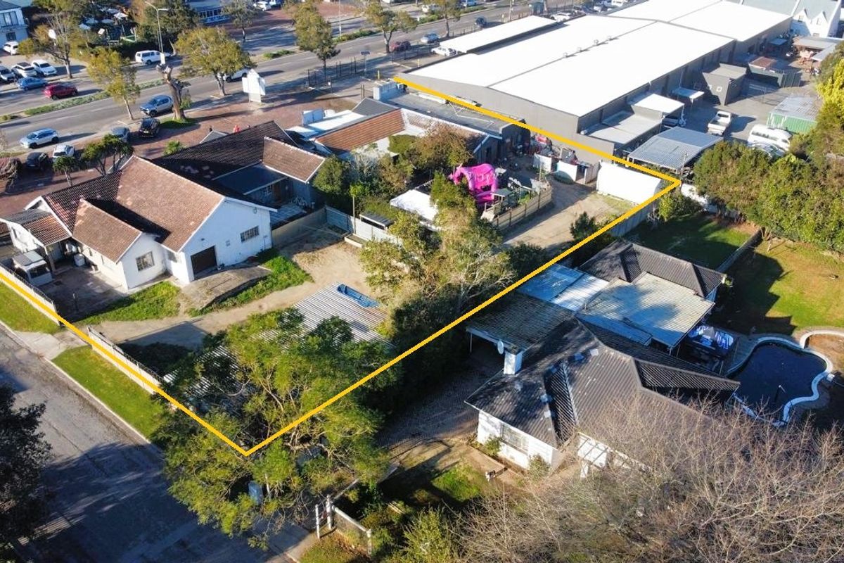 Aerial view of a commercial property site featuring multiple structures, paved driveway access, and surrounding garden areas with boundary fencing.