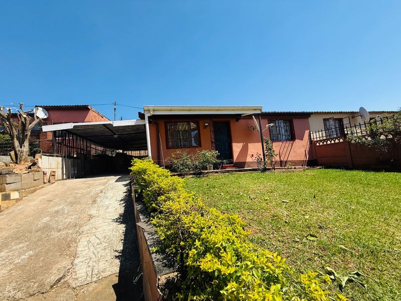 Front view of a single-story house featuring a concrete driveway, attached carport, and a front garden with a boundary wall.