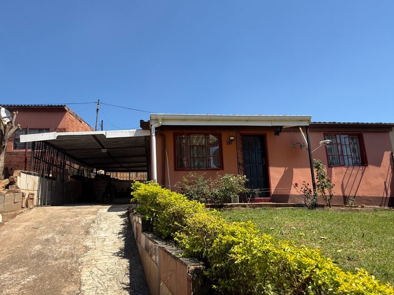Front elevation of a single-story house featuring a concrete driveway, attached carport, and a small front garden with a retaining wall.