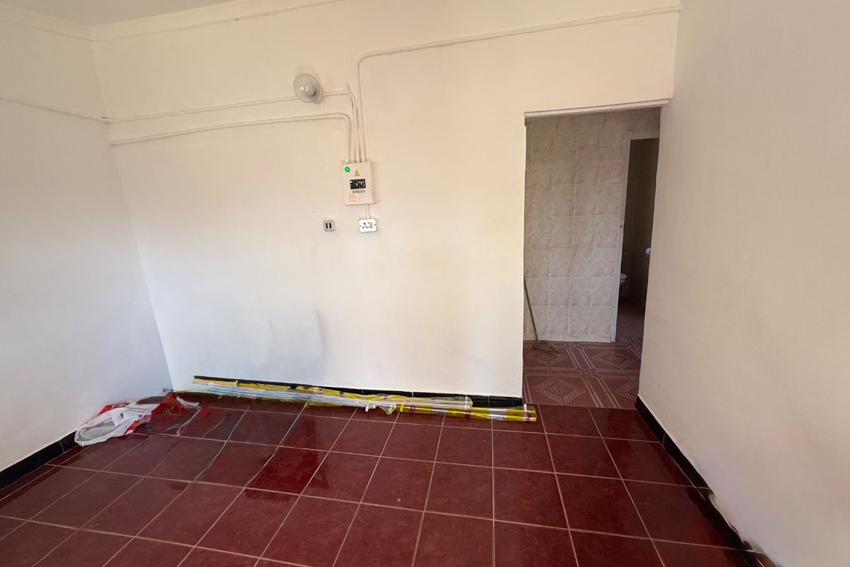 An empty living area featuring red ceramic floor tiles and exposed surface-mounted electrical conduit, leading into an adjacent tiled space.