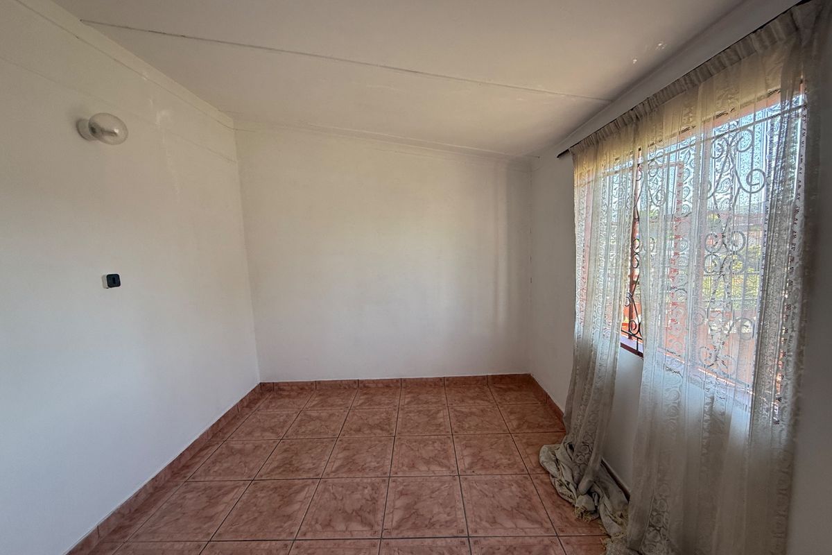 An empty bedroom featuring tiled flooring, a wall-mounted light fixture, and a window fitted with security bars.