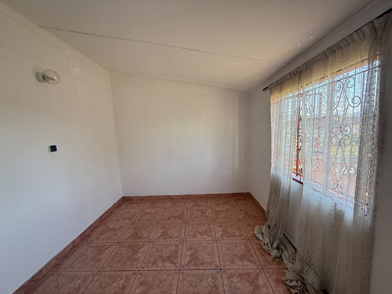 An empty bedroom featuring tiled flooring, a wall-mounted light fixture, and a window fitted with security bars.