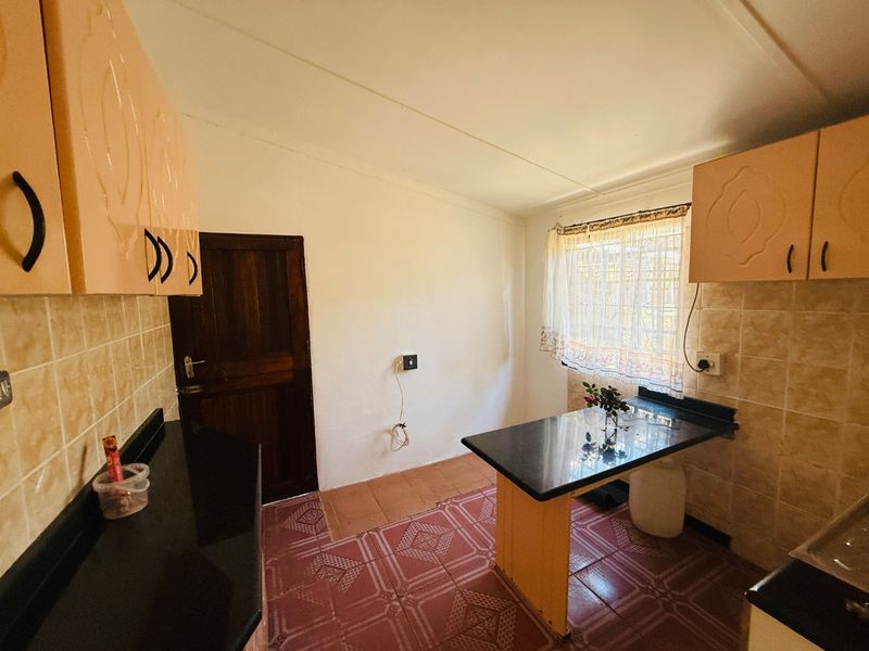 A functional kitchen featuring built-in cabinetry, granite countertops, tiled backsplash, and tiled flooring, offering a practical layout with natural light.