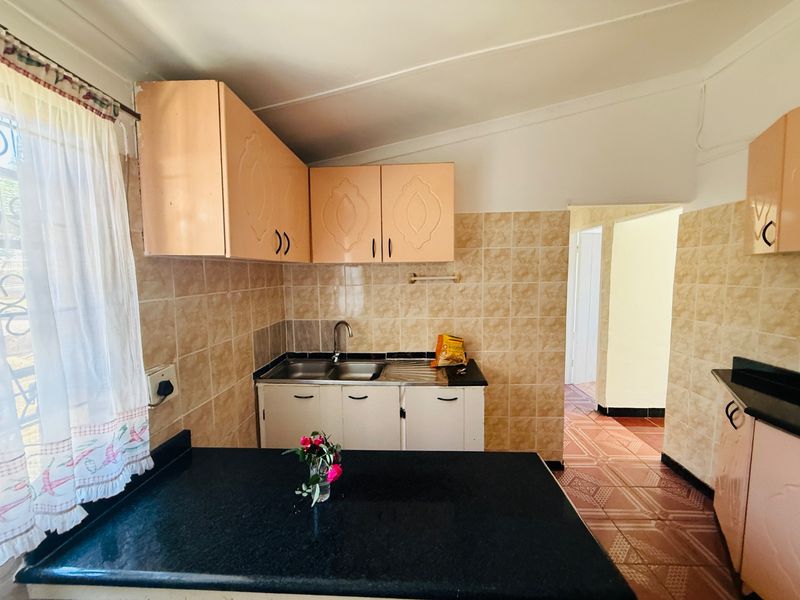 A functional kitchen featuring built-in cabinetry, granite countertops, a double bowl sink, and tiled splashbacks with direct access to the hallway.
