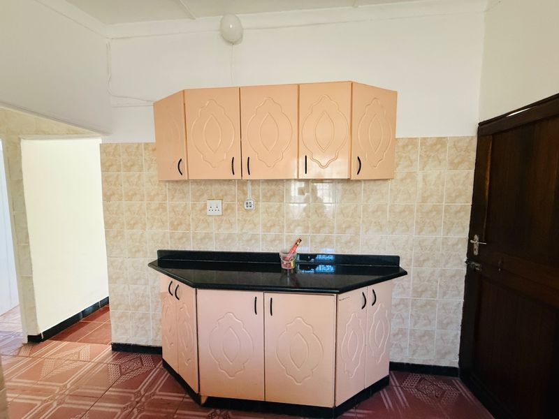 A compact kitchen area featuring dated built-in cabinetry, a dark granite countertop, and neutral tiled backsplash and flooring.