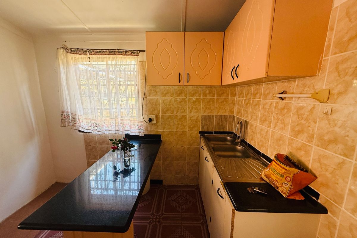 A functional kitchen featuring granite countertops, built-in cabinetry, a stainless steel sink, and tiled backsplash, offering a practical layout with natural light.