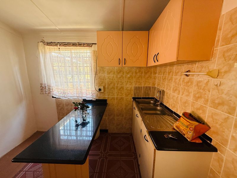 A functional kitchen featuring granite countertops, built-in cabinetry, a stainless steel sink, and tiled backsplash, offering a practical layout with natural light.
